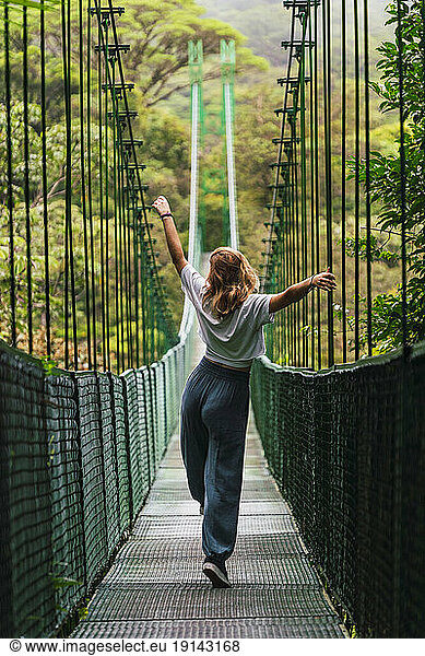 Carefree woman with arms outstretched walking on bridge