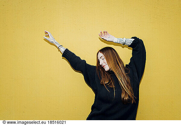 Carefree woman with arms raised enjoying in front of yellow wall
