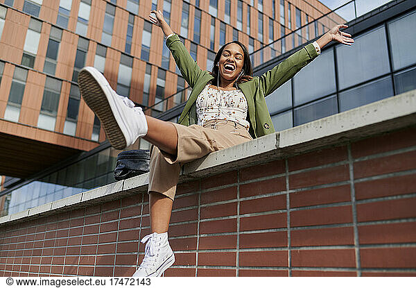 Carefree woman with arms raised on wall in city