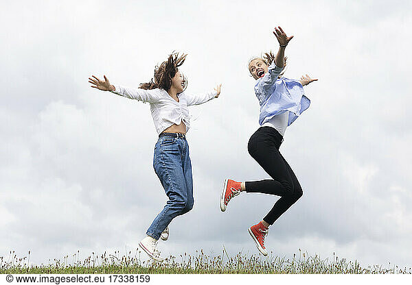 Carefree young female friends jumping on grass