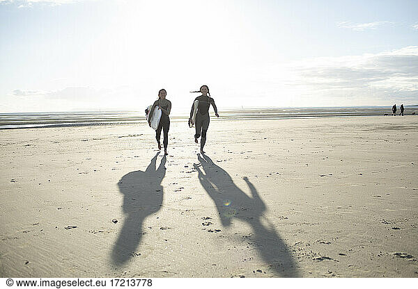 Carefree young female surfers running on sunny beach with surfboards