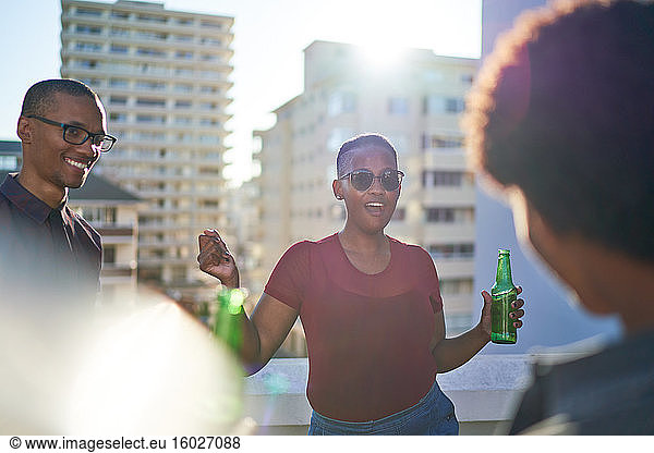 Carefree young friends dancing and drinking beer on sunny rooftop