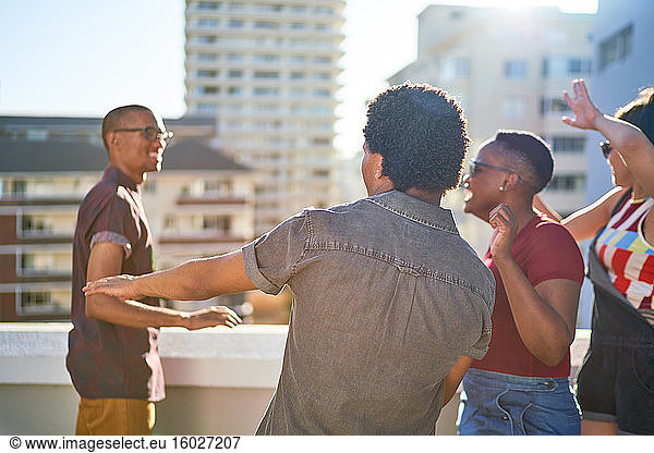 Carefree young friends dancing on sunny urban rooftop