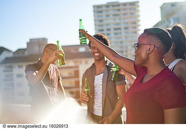 Carefree young friends drinking beer on sunny urban balcony