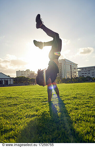 Carefree young man doing handstand in sunny park grass