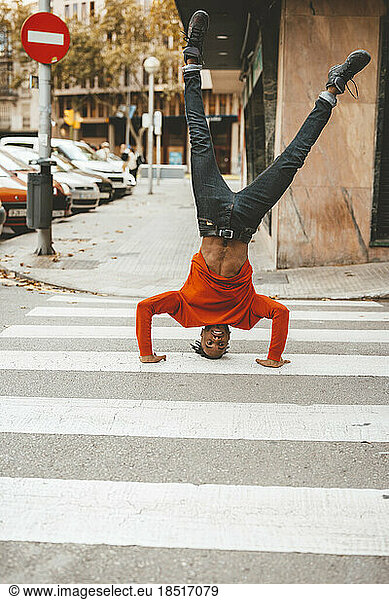 Carefree young man doing headstand on zebra crossing