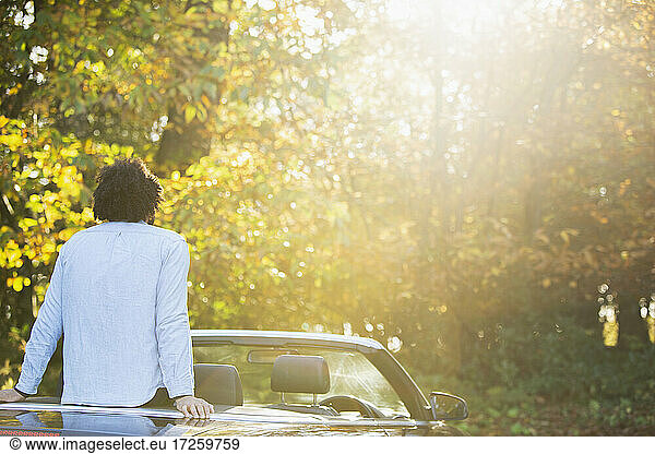 Carefree young man in convertible in sunny idyllic autumn park