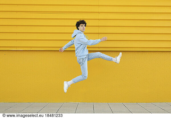 Carefree young man jumping in front of yellow wall