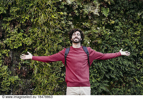 Carefree young man with arms outstretched standing in front of plants