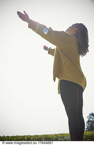 Carefree young woman basking in sunshine with arms outstretched