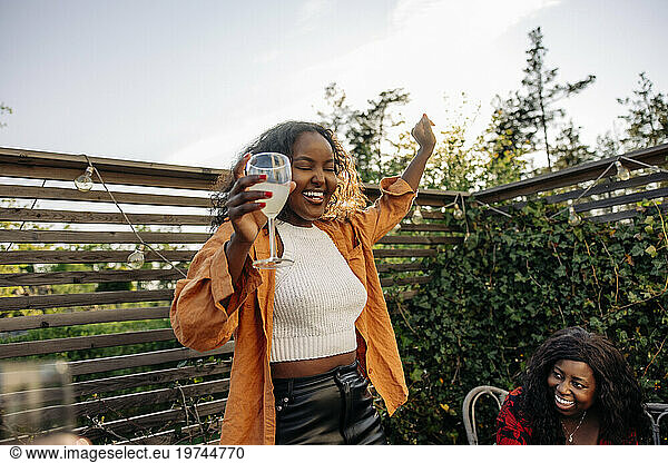 Carefree young woman dancing while holding drink glass during dinner party