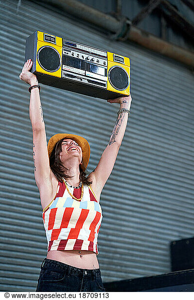 Carefree young woman holding boom box overhead in alley
