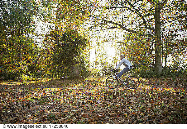 Carefree young woman riding bicycle through autumn leaves in park