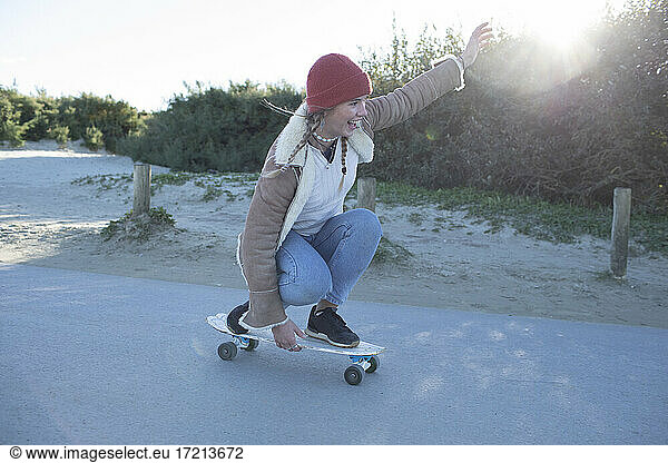 Carefree young woman skateboarding on beach path