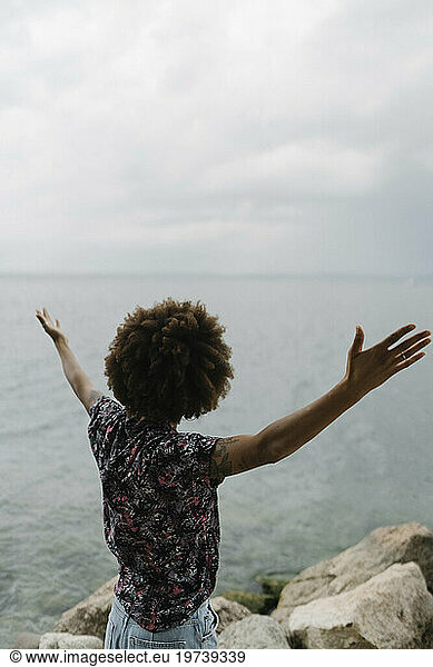Carefree young woman with arms outstretched in front of lake