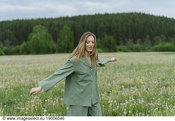 Carefree young woman with arms outstretched walking on dandelion field
