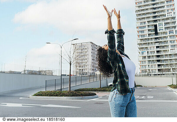 Carefree young woman with arms raised dancing on parking lot