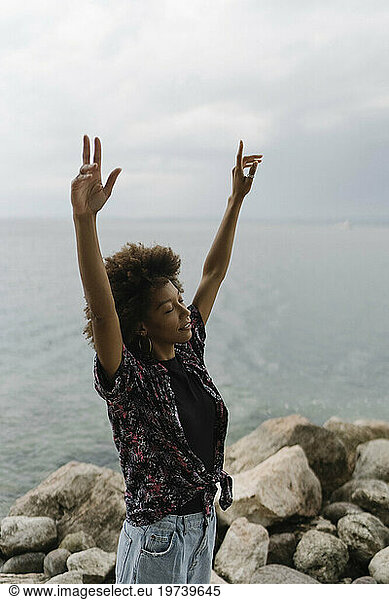 Carefree young woman with arms raised standing in front of lake