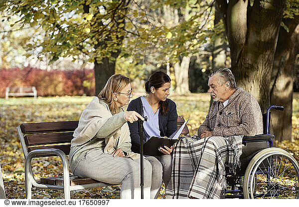 Caretaker discussing documents with disabled man and senior woman at park