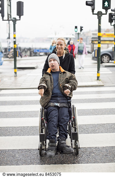 Caretaker pushing disabled man on wheelchair while crossing road