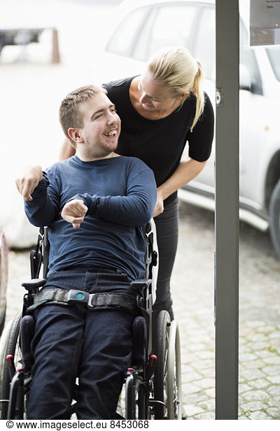 Caretaker talking to disabled man on wheelchair outdoors