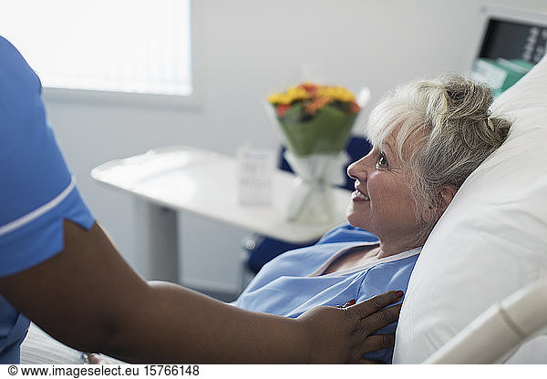 Caring female nurse comforting senior woman resting in hospital bed