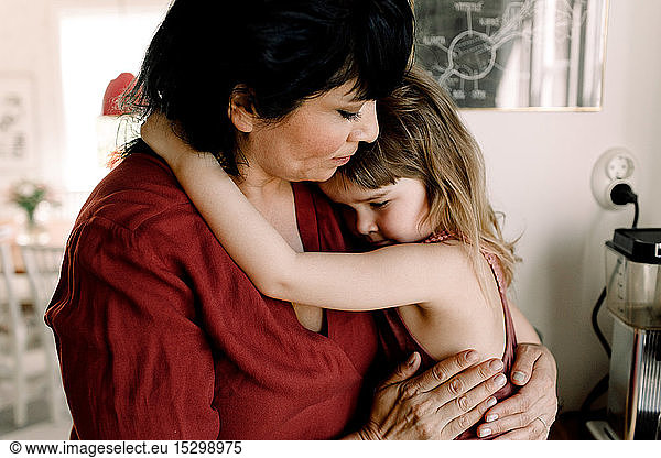Caring mother holding sad daughter while standing at home