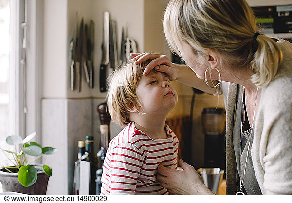 Caring mother looking at daughter's bruised eye in kitchen