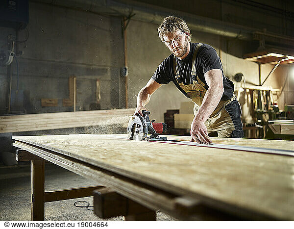 Carpenter cutting oriented strand board with circular saw in workshop