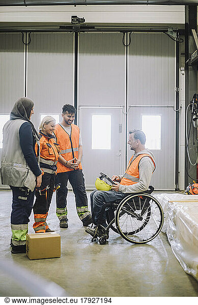 Carpenter sitting on wheelchair discussing with male and female colleagues in warehouse