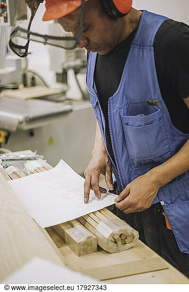 Carpenter worker reading blueprint while working in warehouse