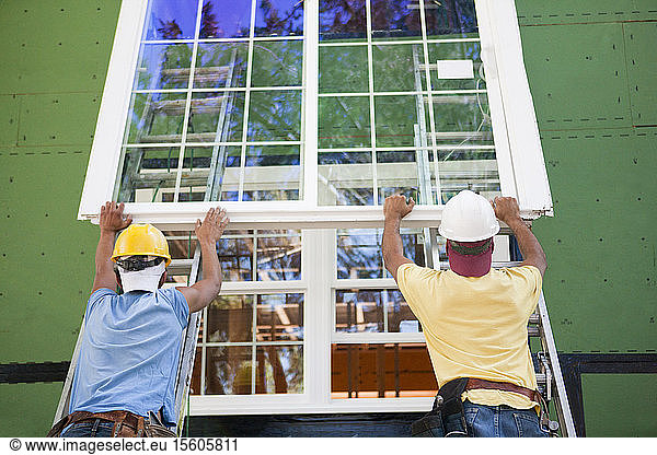 Carpenters positioning a large window frame on a house under construction