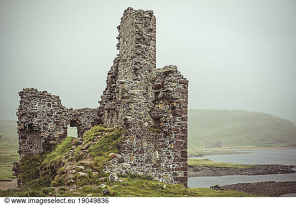 Castle ruins on moody loch water surrounded by misty mountains