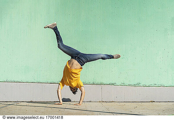 Casual man doing handspring in front of green wall