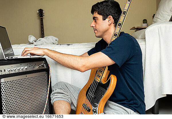 Casual man using a laptop to learn to play electric bass at home.