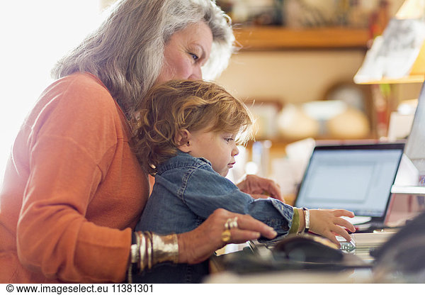 Caucasian baby boy in lap of grandmother using computer