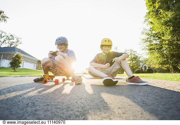 Caucasian boys sitting on skateboards and using cell phones