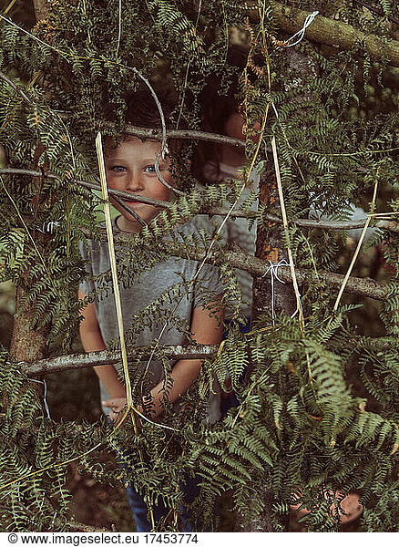 caucasian child in a hut made of branches and leaves