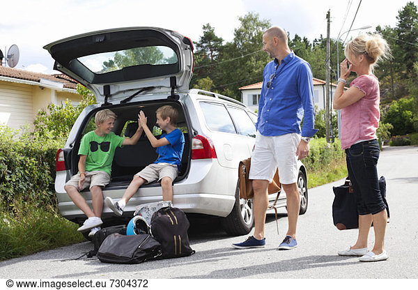 Caucasian couple looking at happy sons sitting in car trunk before going for picnic