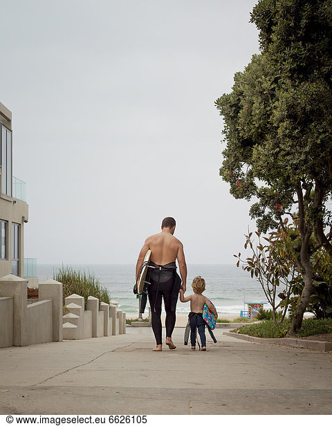 Caucasian father and son in wetsuits walking toward the ocean