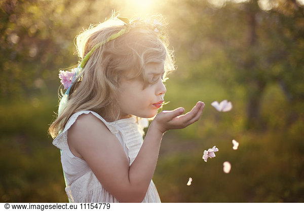 Caucasian girl blowing flower petals outdoors