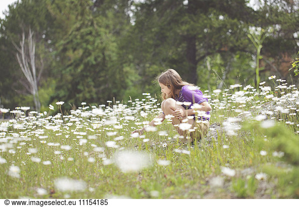 Caucasian girl crouching in field of flowers