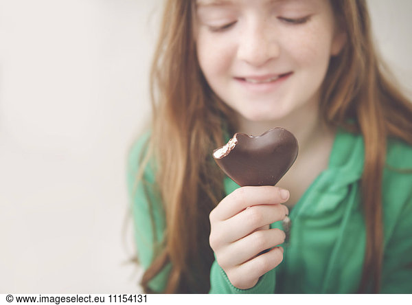 Caucasian girl eating heart-shaped chocolate