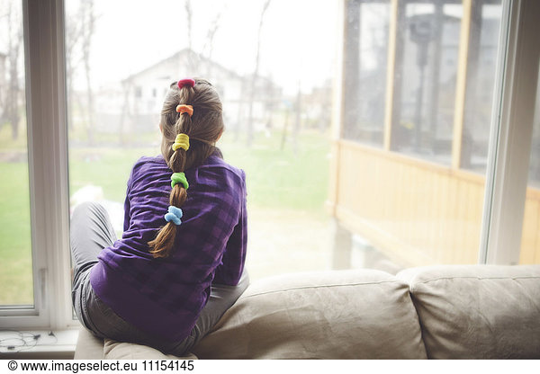 Caucasian girl looking out living room window