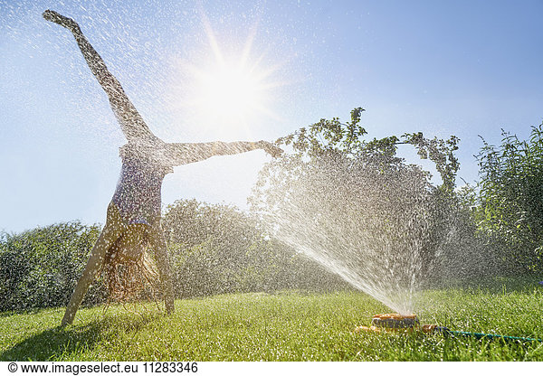 Caucasian girl performing cartwheel through backyard sprinkler