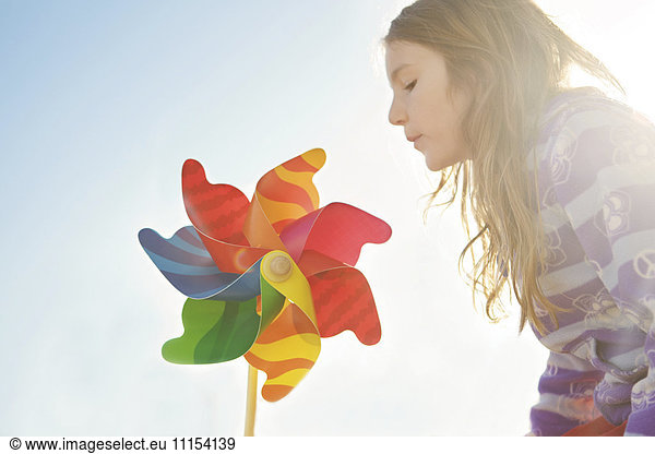 Caucasian girl playing with pinwheel under blue sky