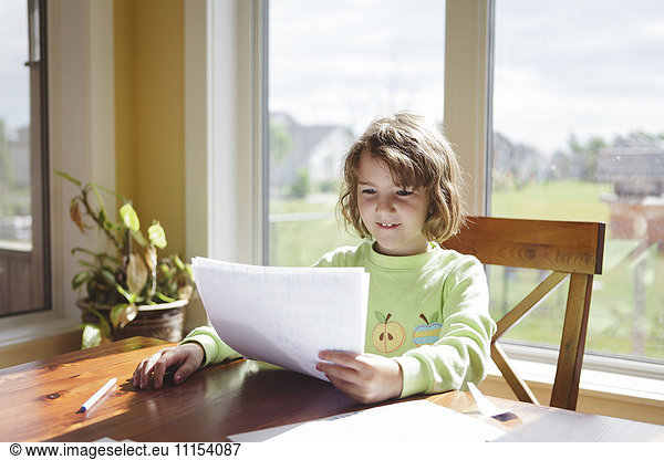 Caucasian girl reading papers at table