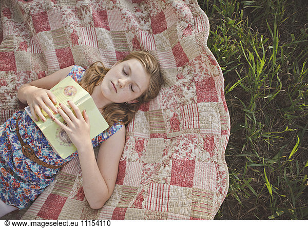 Caucasian girl sleeping with book on blanket