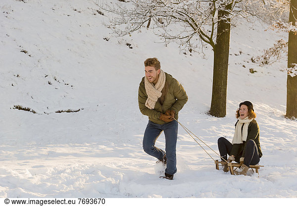 Caucasian man pulling girlfriend on sled in snow
