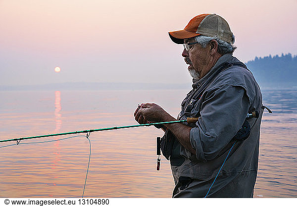 Caucasian man tying a fly on his fly fishing line while fishing for salmon and searun cutthroat trout